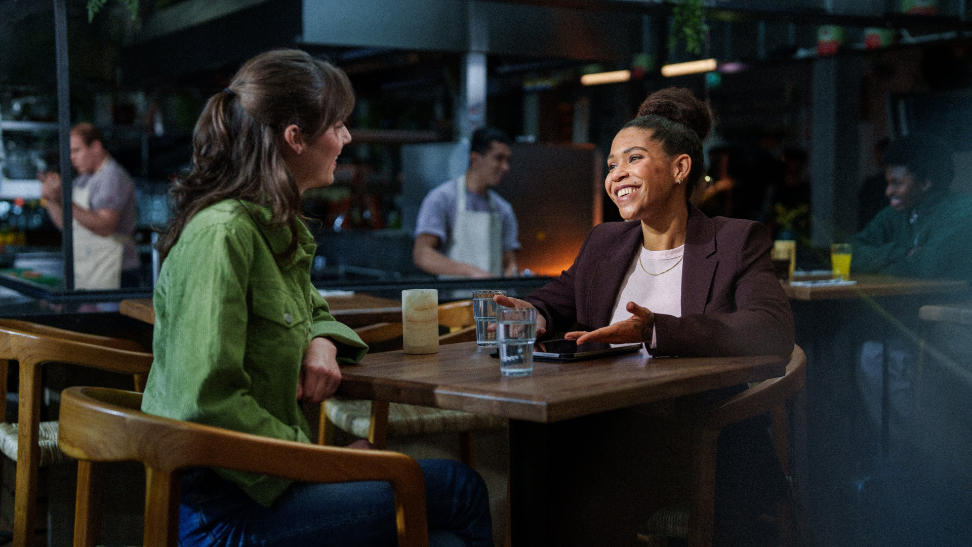 en vrouwelijke Assistent Horeca Manager in een informeel en enthousiast gesprek met een potentiële nieuwe medewerker in een moderne horecaomgeving op Schiphol.