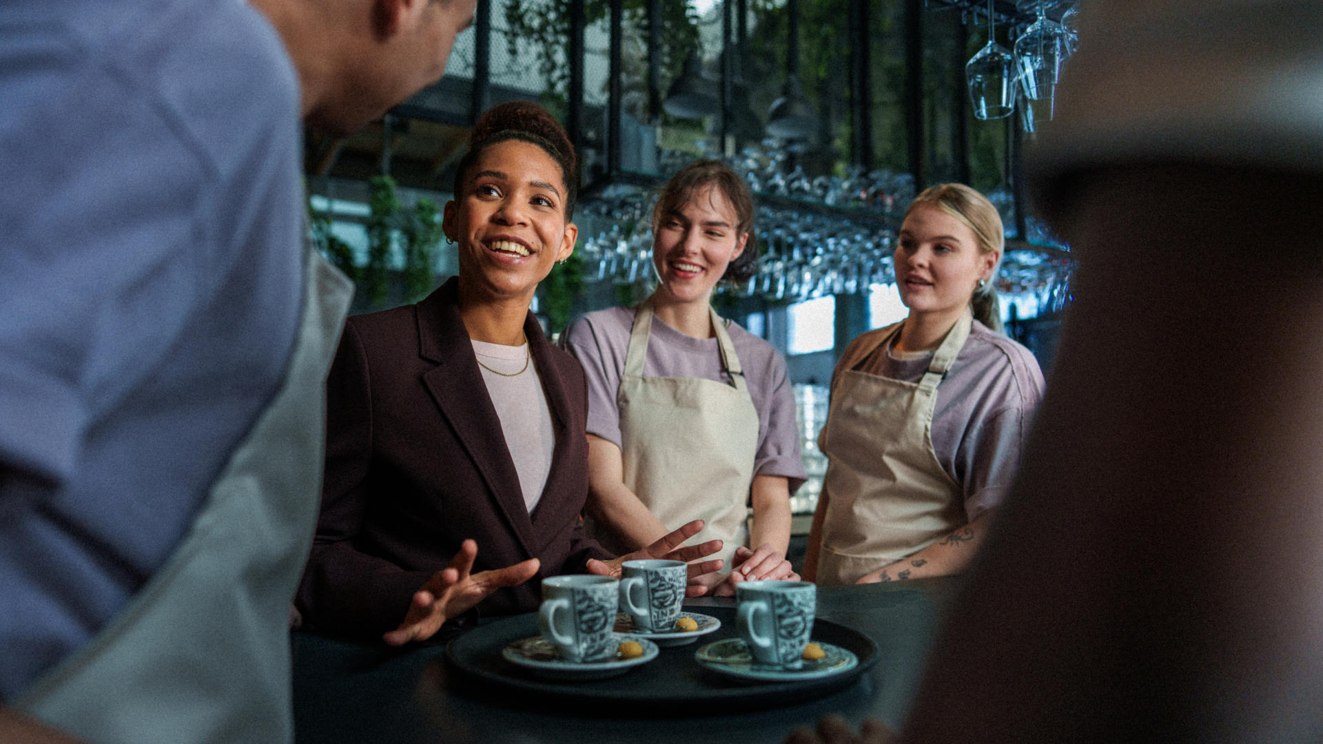 Een glimlachende Assistent Horeca Manager die op de werkvloer een jonge medewerker coacht en ondersteunt bij de dagelijkse horeca-werkzaamheden.