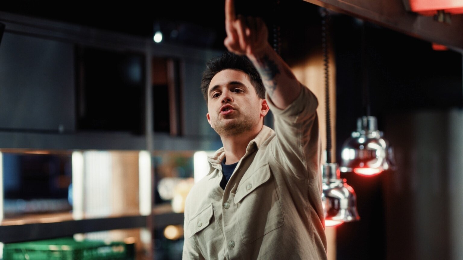 Een man geeft duidelijke instructies in de keuken terwijl hij zijn hand omhoog houdt, onder warme keukenverlichting.