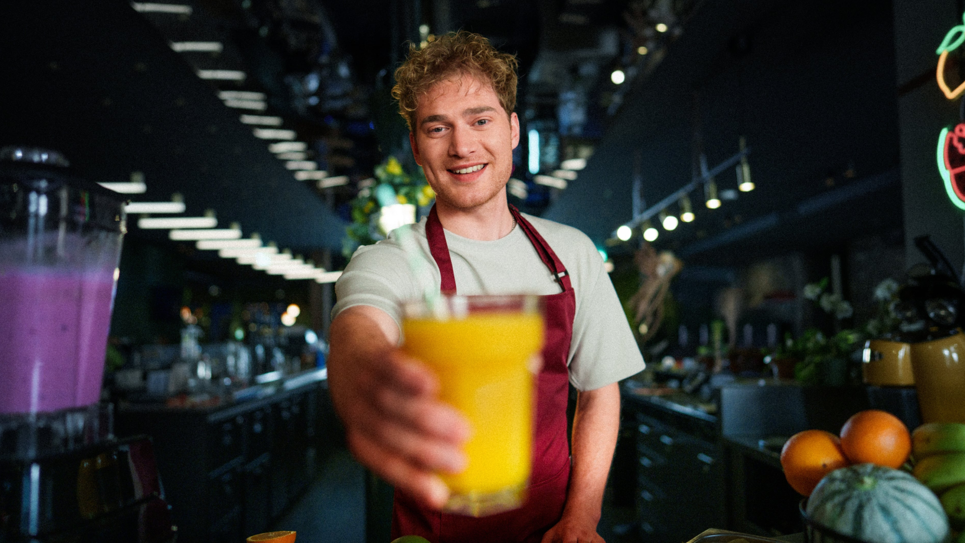 Een enthousiaste medewerker achter de counter die met een glimlach een glas verse jus d'orange aanreikt aan de kijker.